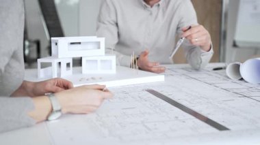 Mimarlık uzmanları proje toplantısı sırasında çağdaş bir ofis ortamında tasarım ayrıntılarını rafine etmek için bir cetvel kullanarak projeler ve ev ölçeği modeli üzerinde işbirliği yaparlar.
