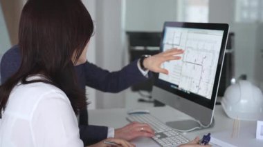 Yeni bir inşaat projesi üzerinde çalışan tasarım uzmanları, bir masaüstü bilgisayarında plan ve mimari çizimleri inceliyorlar. İş ve mimari kavramı