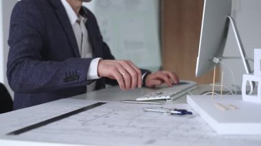 Modern ofiste klavyede yazan profesyonel mimar, planlar, ölçek modelleri ve tasarım araçları ile çevrili, planlama projesi. İş ve mimari kavramı