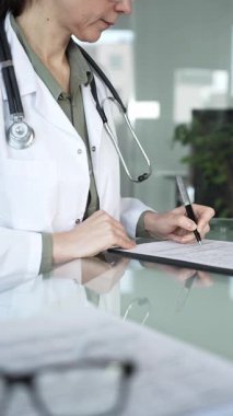 Masasında steteskop yazılı beyaz önlüklü doktor muayene sırasında hasta bilgilerini belgeliyor. İlaç ve sağlık hizmetleri kavramı