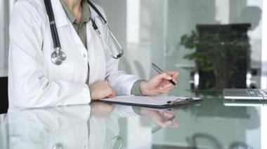 Masasında steteskop yazılı beyaz önlüklü doktor muayene sırasında hasta bilgilerini belgeliyor. İlaç ve sağlık hizmetleri kavramı