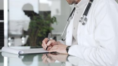 Steteskoplu beyaz önlüklü bir doktor klinikte tıbbi bakım ve profesyonel hizmetler sağlayan bir belge hazırlıyor. Tıp, sağlık ve bilim konsepti