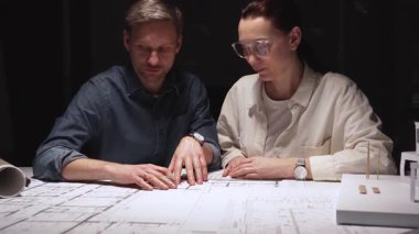 Mimari planlar ve kağıt ev modeli üzerinde yoğunlaşan profesyoneller, gelecekte bir konut veya ticari kalkınma için inşaat unsurlarını dikkatle ölçüyor ve tartışıyor