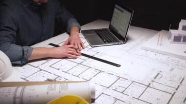 Yeni bir konut geliştirme projesinin planlarını çizen mimar, modern ofis ortamında detaylı ev planları üzerinde çalışarak, inşaat için yenilikçi mimari tasarımlar yaratıyor