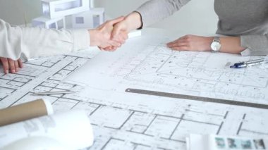 Bir ortaklık kuran iş adamları, mimari planları ve bina modelini el sıkışarak, başarılı bir anlaşmayı ve inşaat endüstrisindeki işbirliğini sembolize ederek,