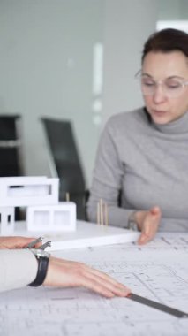 Planlar üzerinde işbirliği yapan mimarlar, kadın bir meslektaşın gözlemlediği gibi planları ölçmek için pusula kullanan bir erkek tasarımcı, proje detayları ve mimari tasarımı tartışan,