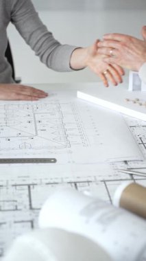 Bir ortaklık kuran iş adamları, mimari planları ve bina modelini el sıkışarak, başarılı bir anlaşmayı ve inşaat endüstrisindeki işbirliğini sembolize ederek,