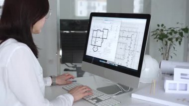 Mimari planlar ve bina modelleriyle çevrili bir masada, bir masaüstü bilgisayarı ve klavyeyi kullanarak gözlük takan mimar. İş ve mimari kavramı