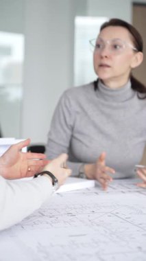 Planlar üzerinde işbirliği yapan mimarlar, kadın bir meslektaşın gözlemlediği gibi planları ölçmek için pusula kullanan bir erkek tasarımcı, proje detayları ve mimari tasarımı tartışan,