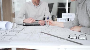 Mimari planlar ve inşaat planları üzerinde işbirliği yapan mimarlar, mühendislik projesinin detaylarını tartışan, bir ofiste tasarım araçları ve dijital tablet kullanan mimarlar