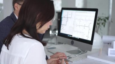 Yeni bir inşaat projesi üzerinde çalışan tasarım uzmanları, bir masaüstü bilgisayarında plan ve mimari çizimleri inceliyorlar. İş ve mimari kavramı