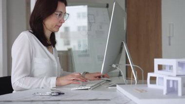 Profesyonel kadın, ofis çalışma alanındaki masasında teknoloji ve fiziksel modeller kullanarak mimari tasarımlar yaratmaya odaklandı. İş ve mimari kavramı