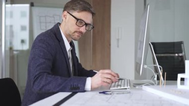 Erkek mimar, mimari bir stüdyoda yeni yapılar ve modeller tasarlayarak bilgisayar ekranına ve planlara derinden odaklanmıştır. İş ve mimari kavramı