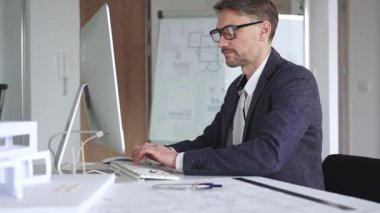 Erkek mimar, mimari bir stüdyoda yeni yapılar ve modeller tasarlayarak bilgisayar ekranına ve planlara derinden odaklanmıştır. İş ve mimari kavramı