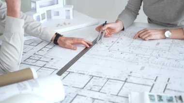 Mimarlar karmaşık bir masa üzerinde ayrıntılı planlar ve beyaz ölçekli bir model üzerinde işbirliği yaparlar, bir inşaat projesi planlarlar ve profesyonel bir tasarım toplantısı sırasında fikirleri paylaşırlar, kapatırlar