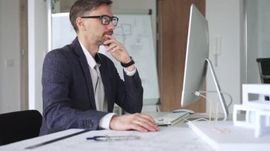 Erkek mimar, mimari bir stüdyoda yeni yapılar ve modeller tasarlayarak bilgisayar ekranına ve planlara derinden odaklanmıştır. İş ve mimari kavramı