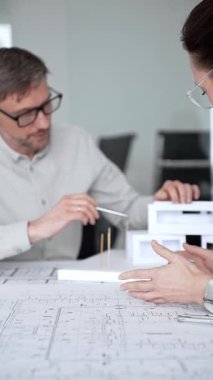 Mimari planlar ve inşaat planları üzerinde işbirliği yapan mimarlar, mühendislik projesinin detaylarını tartışan, bir ofiste tasarım araçları ve dijital tablet kullanan mimarlar