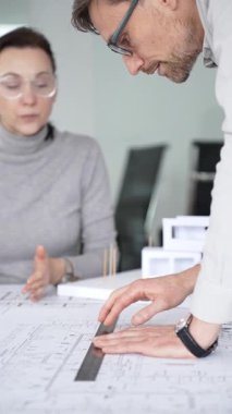 Mimarlar inşaat planlarını ve 3D yapı modelini gözden geçiriyorlar, profesyonel ofis ortamında yeni bir mimari proje üzerinde çalışırken ayrıntılı bir tasarım tartışmasına girişiyorlar.