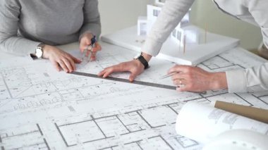 Mimarlar küçük bir ev modelinin ayrıntılı planlarını çizer ve ölçerler, bir konut tasarımı projesi için kesin takım çalışması, planlama ve işbirliği vurgulanır, kapat
