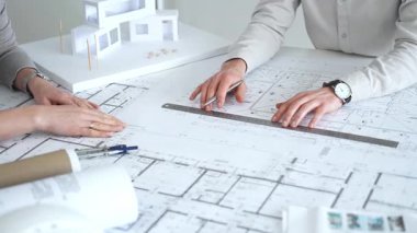 Mimarlar karmaşık bir masa üzerinde ayrıntılı planlar ve beyaz ölçekli bir model üzerinde işbirliği yaparlar, bir inşaat projesi planlarlar ve profesyonel bir tasarım toplantısı sırasında fikirleri paylaşırlar, kapatırlar