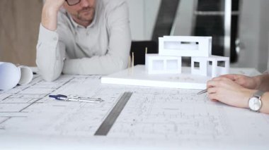 Mimarlık uzmanları proje toplantısı sırasında çağdaş bir ofis ortamında tasarım ayrıntılarını rafine etmek için bir cetvel kullanarak projeler ve ev ölçeği modeli üzerinde işbirliği yaparlar.