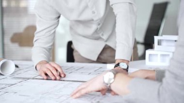 Mimarlar yeni bina tasarımını tartışıyor, ayrıntılı planların üzerinde bir pusula tutuyor, modern bir ofis düzeninde ev mimarisi modeliyle proje geliştirmede işbirliği yapıyor,