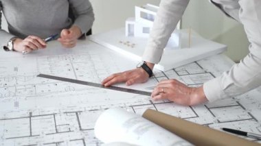 Mimarlar küçük bir ev modelinin ayrıntılı planlarını çizer ve ölçerler, bir konut tasarımı projesi için kesin takım çalışması, planlama ve işbirliği vurgulanır, kapat