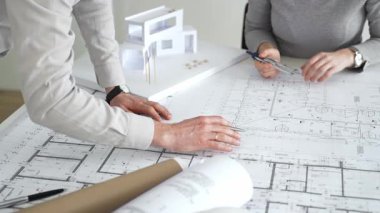 Mimarlar küçük bir ev modelinin ayrıntılı planlarını çizer ve ölçerler, bir konut tasarımı projesi için kesin takım çalışması, planlama ve işbirliği vurgulanır, kapat