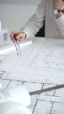 Mimarlar detaylı planlar ve beyaz bir masanın üzerinde bir ölçek modeli etrafında toplanarak, modern bir konut projesinde işbirliği yaparken planları analiz ediyor, araçlar ve belgeler çiziyor ve kapatıyorlar.