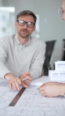 Mimari planlar ve inşaat planları üzerinde işbirliği yapan mimarlar, mühendislik projesinin detaylarını tartışan, bir ofiste tasarım araçları ve dijital tablet kullanan mimarlar