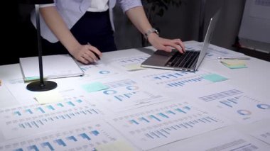 Ekonomik raporları ve hesap tablolarını bir masada inceleyen, stratejik planlama ve yatırım kararları için notlar alırken çizelgeleri ve dizüstü bilgisayarların grafiklerini analiz eden iş adamı.