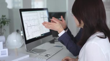 Yeni bir inşaat projesi üzerinde çalışan tasarım uzmanları, bir masaüstü bilgisayarında plan ve mimari çizimleri inceliyorlar. İş ve mimari kavramı