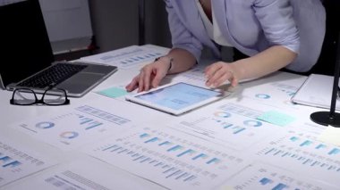 Ekonomik raporları ve hesap tablolarını bir masada inceleyen, stratejik planlama ve yatırım kararları için notlar alırken çizelgeleri ve dizüstü bilgisayarların grafiklerini analiz eden iş adamı.