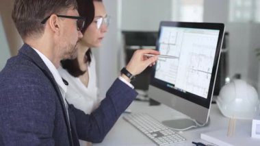 Mimarlar ve mühendisler birlikte çalışarak modern bir masaüstü bilgisayar ekranının planlarını tartışıyorlar. Takım çalışması ve tasarım süreci gösteriliyor. İş ve mimari kavramı