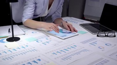 Ekonomik raporları ve hesap tablolarını bir masada inceleyen, stratejik planlama ve yatırım kararları için notlar alırken çizelgeleri ve dizüstü bilgisayarların grafiklerini analiz eden iş adamı.