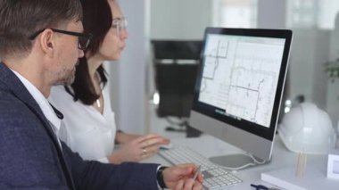 Mimarlar ve mühendisler birlikte çalışarak modern bir masaüstü bilgisayar ekranının planlarını tartışıyorlar. Takım çalışması ve tasarım süreci gösteriliyor. İş ve mimari kavramı