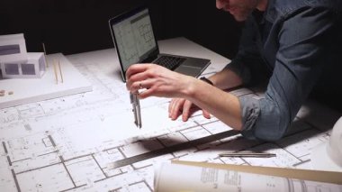 Yeni bir konut geliştirme projesinin planlarını çizen mimar, modern ofis ortamında detaylı ev planları üzerinde çalışarak, inşaat için yenilikçi mimari tasarımlar yaratıyor