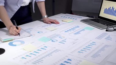 İş kadını kurumsal mali verileri analiz ediyor, istatistik ve pazar eğilimlerini yönetiyor, belgeleri inceliyor, yatırım stratejisi planlıyor, ofiste yıllık bir rapor üzerinde çalışıyor