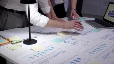 Meşgul profesyonel yönetici, çok sayıda finansal raporu ve iş belgelerini aktif olarak analiz ederek, bir dizüstü bilgisayar ve kalemle istatistikleri gözden geçirmek için, parlak bir şekilde aydınlatılmış bir masa üzerinde çalışmaktadır.