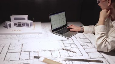 Kadın mimar konut planları tasarlıyor, cetvel ve kalemle planlar hazırlıyor, dizüstü bilgisayar teknolojisi ve mühendislik araçları kullanarak modern ev yapımı için bir model geliştiriyor.