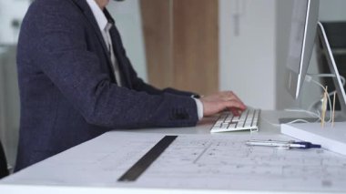 Modern ofiste klavyede yazan profesyonel mimar, planlar, ölçek modelleri ve tasarım araçları ile çevrili, planlama projesi. İş ve mimari kavramı