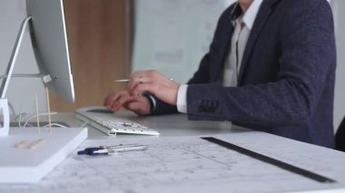 Modern ofiste klavyede yazan profesyonel mimar, planlar, ölçek modelleri ve tasarım araçları ile çevrili, planlama projesi. İş ve mimari kavramı