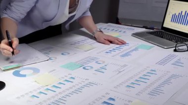 Ekonomik raporları ve hesap tablolarını bir masada inceleyen, stratejik planlama ve yatırım kararları için notlar alırken çizelgeleri ve dizüstü bilgisayarların grafiklerini analiz eden iş adamı.