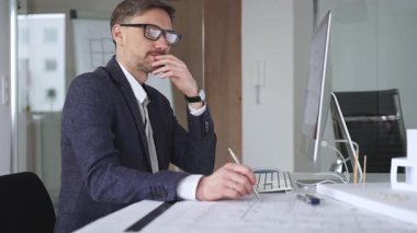 Profesyonel mimar, bir masada oturmuş proje geliştirmeyi düşünürken planlar ve tasarım planlarını analiz ediyor. İş ve mimari kavramı