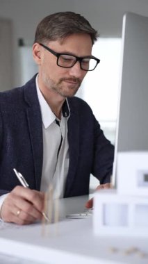 Planlar ve mimari model üzerinde çalışan mimar, ofisteki bilgisayar yazılımını kullanarak yeni bir bina projesi planlıyor. İş ve mimari kavramı