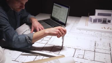 Yeni bir konut geliştirme projesinin planlarını çizen mimar, modern ofis ortamında detaylı ev planları üzerinde çalışarak, inşaat için yenilikçi mimari tasarımlar yaratıyor