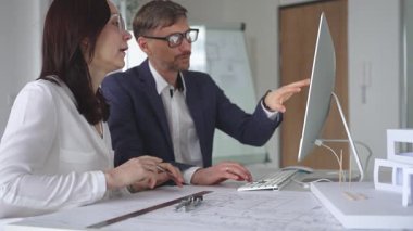 Mimarlar, modern ofis ortamında tasarım ayrıntıları ve inşaat planlarını tartışan planlar ve ölçekli bir model üzerinde işbirliği yapıyorlar. İş ve mimari kavramı