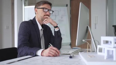 Profesyonel mimar, bir masada oturmuş proje geliştirmeyi düşünürken planlar ve tasarım planlarını analiz ediyor. İş ve mimari kavramı