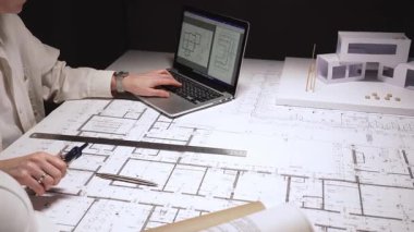 Modern konut projesini tasarlayan mimar, cetvel ve kalemle planlar çizen, fiziksel bir modelle yapıyı görselleştiren, teknik planlar ve geliştirme için dizüstü bilgisayar kullanan