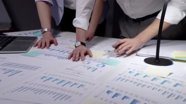 Meşgul profesyonel yönetici, çok sayıda finansal raporu ve iş belgelerini aktif olarak analiz ederek, bir dizüstü bilgisayar ve kalemle istatistikleri gözden geçirmek için, parlak bir şekilde aydınlatılmış bir masa üzerinde çalışmaktadır.